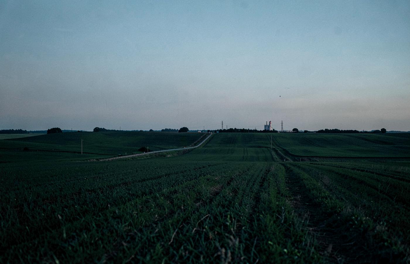 Rolling farmland at dusk with distant natural gas infrastructure